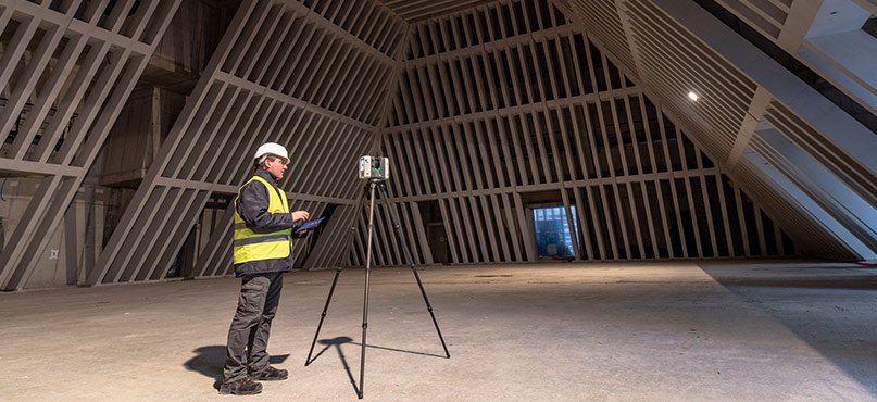 SmartScanz technician operating a tripod-mounted laser scanner on a large commercial site